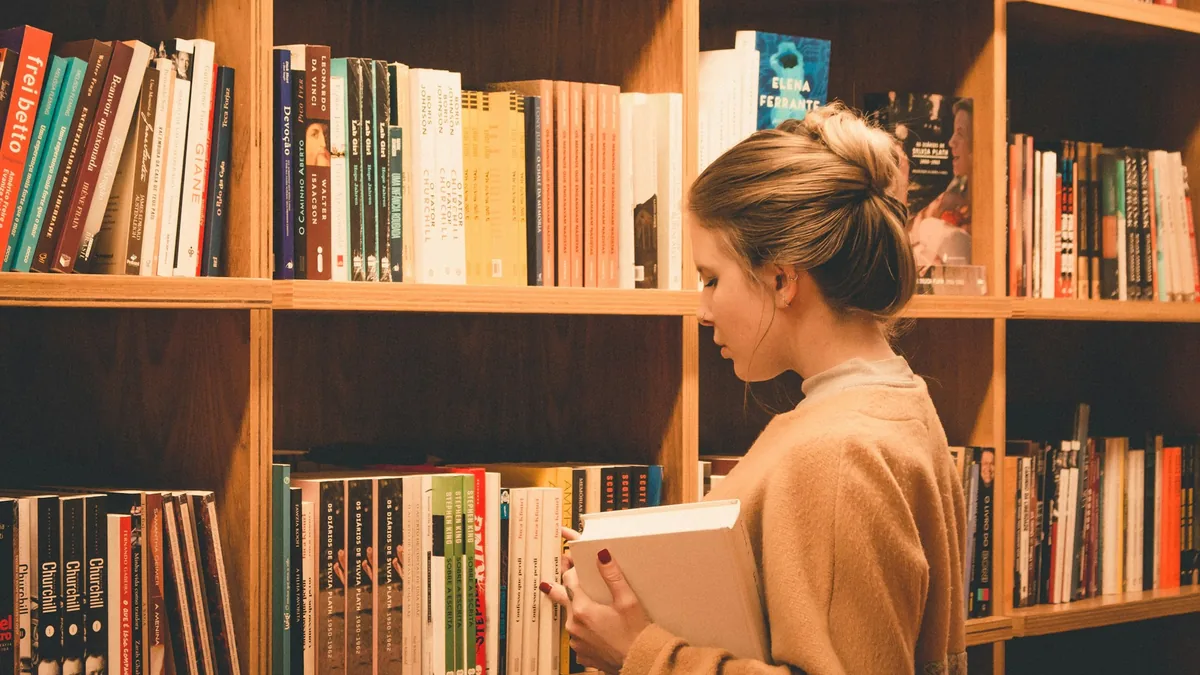 Woman holding a book in front of tall wooden bookshelves