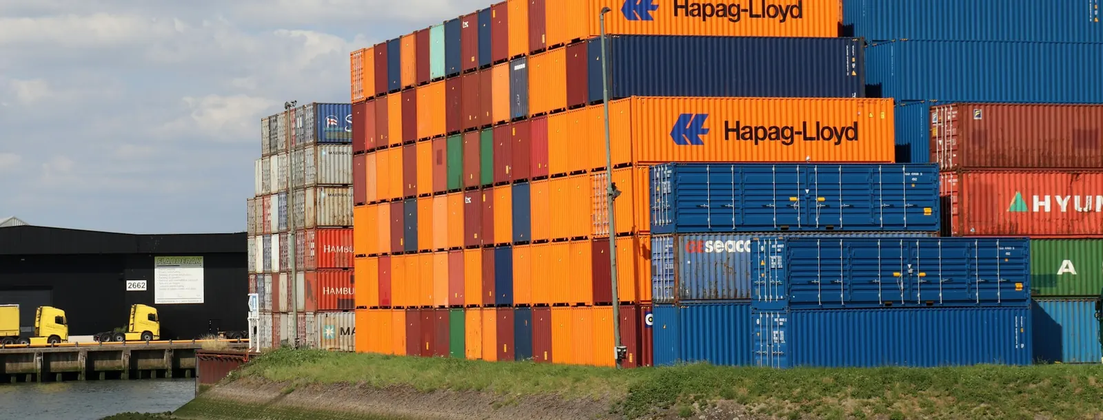 Stacked shipping containers on a quay beside a waterway