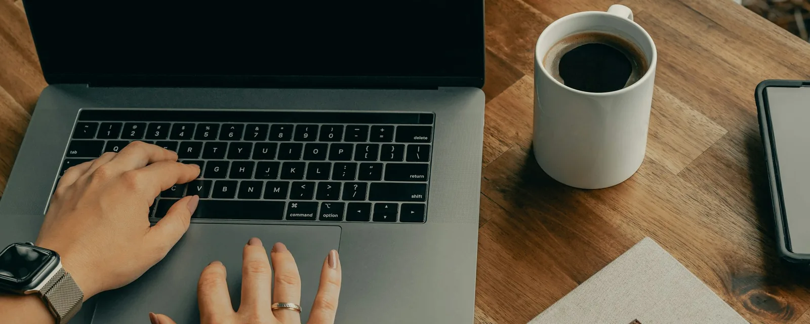 Hands typing on a laptop beside a cup of coffee