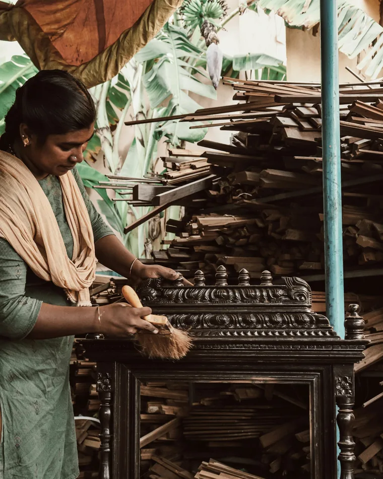 Woman finishing a carved wooden cabinet in a workshop