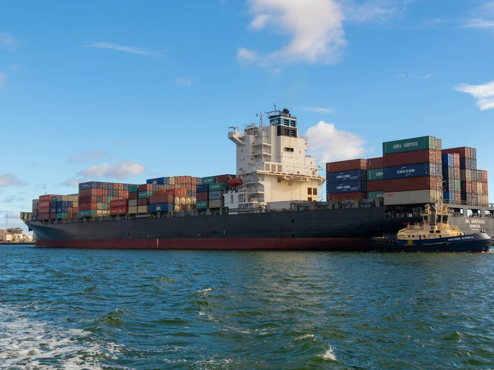 Container ship loaded with stacked containers on open water under a blue sky