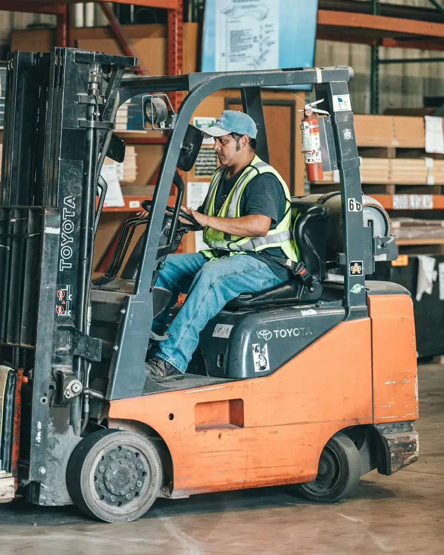Forklift operator in a hi-vis vest driving through a warehouse