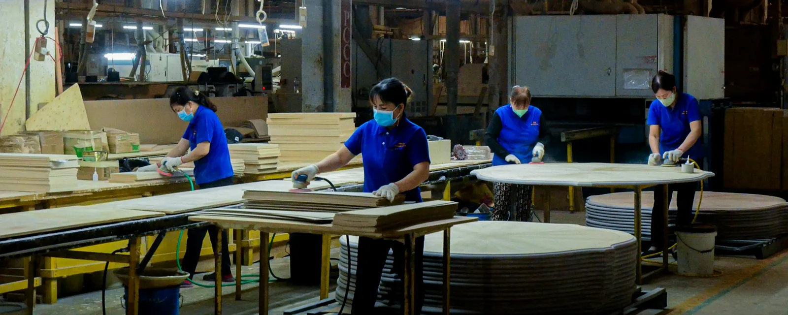 Workers in masks finishing wooden furniture parts in a factory