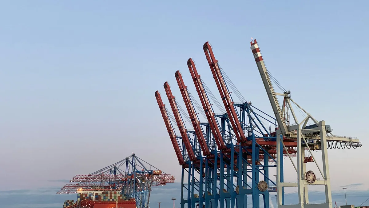 Row of red and blue ship-to-shore container cranes at a port under a clear sky