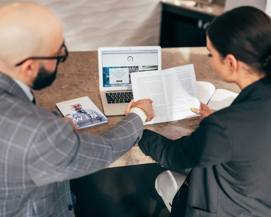 Two people reviewing a printed document at a desk with a laptop