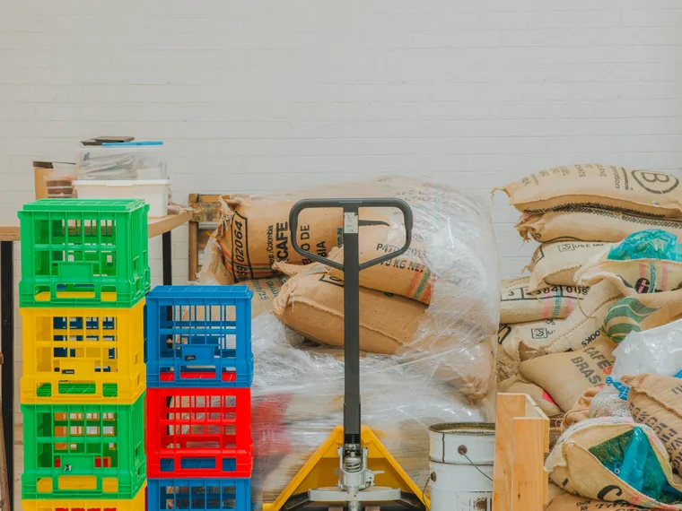 Burlap coffee sacks, crates and a pallet jack in a storeroom