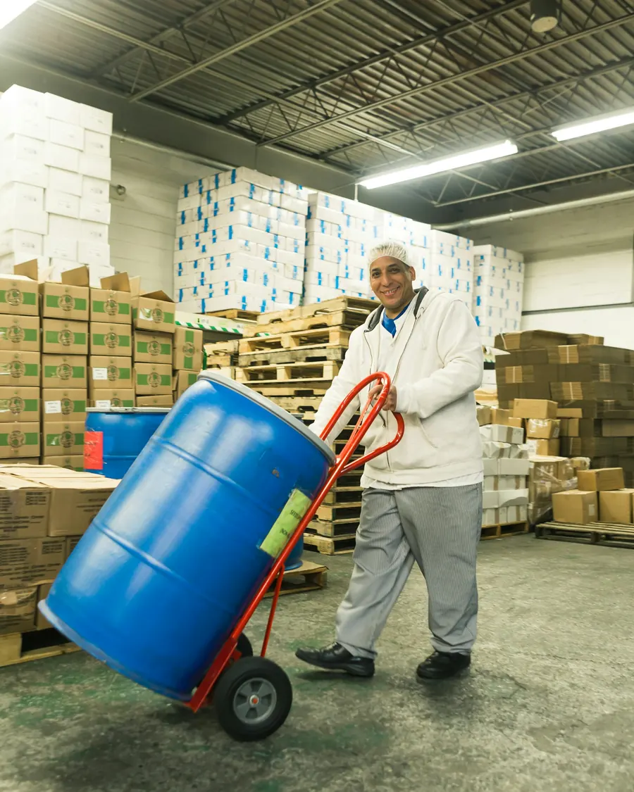 Warehouse worker in a hairnet moving a plastic drum on a hand truck