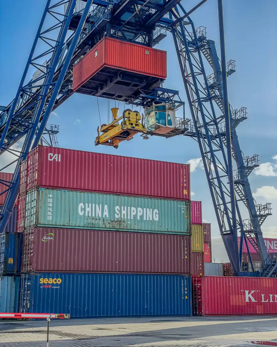 Gantry crane lifting a shipping container above stacked containers