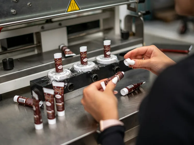 Hands handling small product tubes at a packing machine